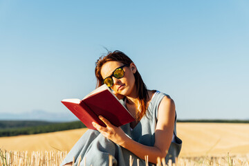 Middle-aged beautiful young woman sitting in cereal field carrying a book with sunglasses. self-care. free time.