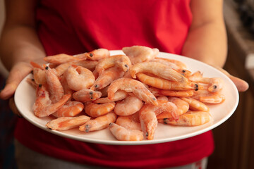 Red frozen shrimps on a white plate in the hands of a girl. Close-up .