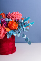 Flowers composition in red hat box on blue background. Bright bouquet in round box. Unusual floral arrangement in oriental style. Vertical