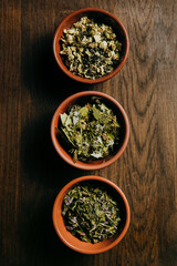 Close up of assortment of dry tea in brown ceramic bowls on a wooden board