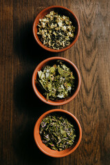 Close up of assortment of dry tea in brown ceramic bowls on a wooden board. Tea ceremony concept