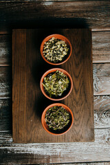 Assortment of dry tea in brown ceramic bowls on a wooden board, in a rustic kitchen