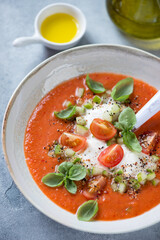 Cold gazpacho soup made of red tomatoes and served with burrata cheese and green basil, close-up, vertical shot