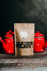 Craft paper pouch bag with herbal tea, and two red teapots behind it