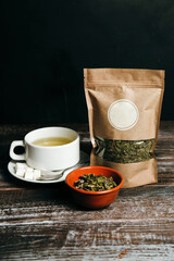A white cup of organic Carpathian tea, squares of sugar, craft paper bag with herbal tea and a...