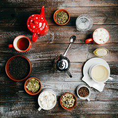 Clock made of teapots, cups, mugs, and bowls with dry black, green, herbal tea leaves with spoon telling the time on a wooden table