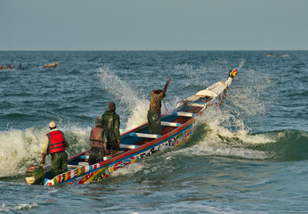 Fototapeta premium Nouakchott. Mauritania. Struggling with the waves of the surf, fishermen daily sail out on special wooden boats with a motor for several days in the open Atlantic Ocean for fishing.