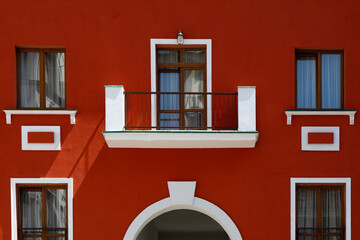 fragment of the facade of a red building with windows, balcony and decorative elements © LariBat