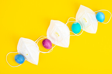 Concept of quarantine at Easter. Decorative eggs and white protective masks on bright background. Social distancing