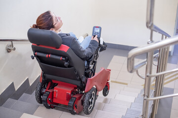 Caucasian woman in electric caterpillar wheelchair climbs up stairs.