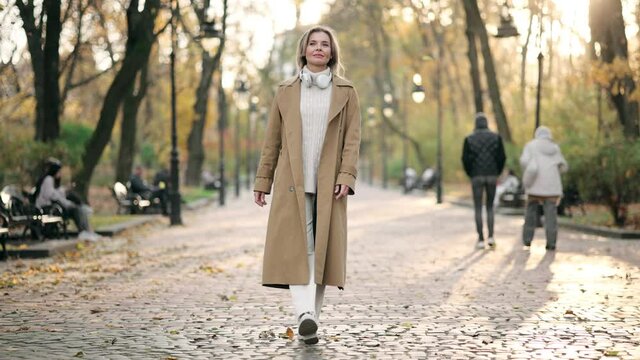 Portrait of an attractive adult blonde woman walking in the park at fall on a sunny day and smiling. Slow-motion 4k footage