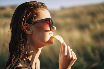 woman in sunglasses eating chips in nature sun