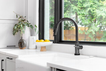 Kitchen sink detail shot in a modern, renovated kitchen with black window frames, a dark faucet, white cabinets, farmhouse sink, and cozy decor. - obrazy, fototapety, plakaty