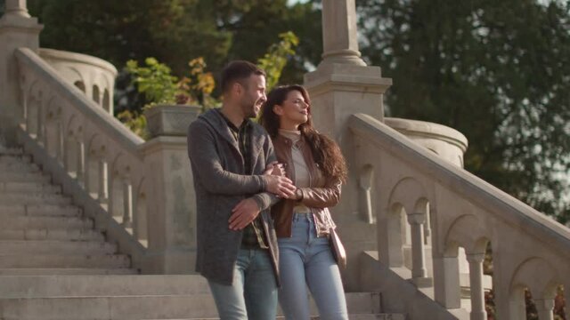 Pretty young couple smiling and talking while strolling down outdoor stairs on autumn day