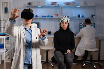 Fototapeta premium Neurologist specialist doctor with virtual reality headset analyzing brain evolution during neuroscience experiment in medical laboratory. Woman patient with eeg scanner having neurology disease