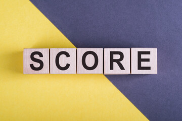 Word SCORE on wooden cubes on yellow - gray background.