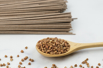 Wooden spoon with buckwheat and Dry Soba buckwheat noodles on the background. Traditional Japanese food, Asian food and healthy eating. Alternative types of flour from different cereals.