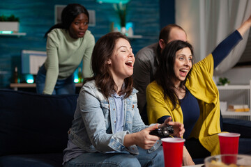 Happy excited women playing videogames using gaming controller winning online competition enjoying spending time in living room. Multi-ethnic friends having fun together during wekeend party