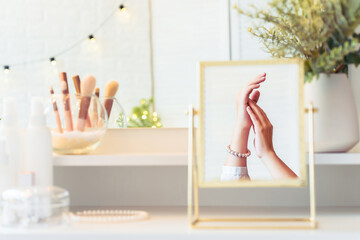 Reflection in table mirror of woman hand  in pearl bracelets on dressing table with make up accessories. Self-Care.