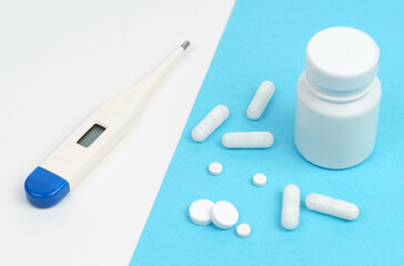 On a white and blue background there is a thermometer, pills, capsules and a white container.