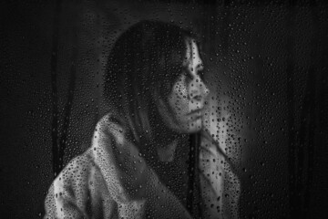 Frau mit Webpelzjacke hinter Glasscheibe im Regen