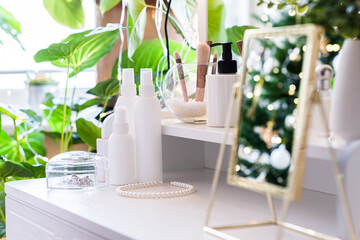 Reflection of christmas tree, light bulbs, in table mirror on woman dressing table with make up accessories