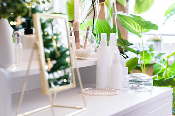 Reflection of christmas tree, light bulbs, in table mirror on woman dressing table with make up accessories