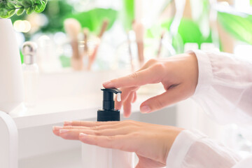 Woman applying daily cream on her hand sitting near dressing table with make up accessories and table mirror.