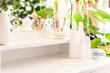 Woman daily cream on dressing table with make up accessories. Reflection of christmas tree, light bulbs in table mirror.