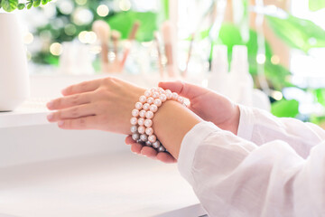 Woman puts on jewelry, pearl bracelets on the hand and  sitting near dressing table with make up accessories.