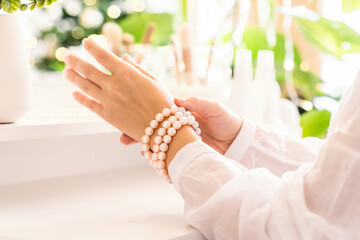 Obraz premium Woman puts on jewelry, pearl bracelets on the hand and sitting near dressing table with make up accessories.