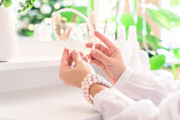 Woman puts on hair band, jewelry, pearl bracelets on the hand and  sitting near dressing table with make up accessories.