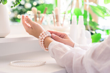 Woman puts on jewelry, pearl bracelets on the hand and  sitting near dressing table with make up accessories.