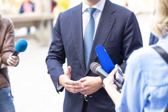 News conference, journalists with microphones interviewing politician or business person during media event