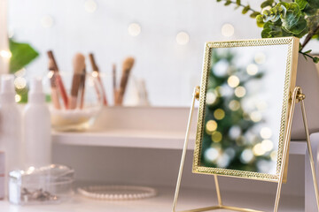 Reflection of christmas tree, light bulbs, in table mirror on woman dressing table with make up accessories