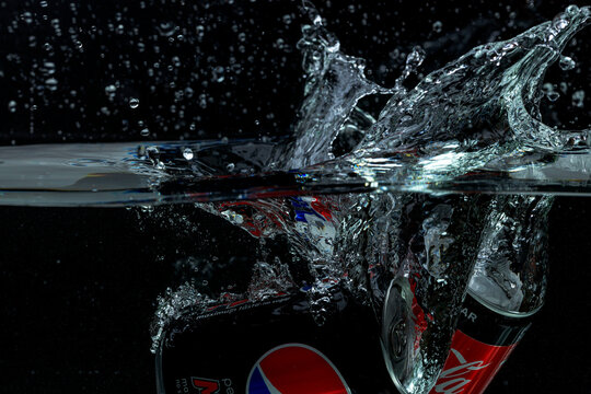Close up view of can of coca cola, pepsi cola falling into water isolation on black background. Sweden.