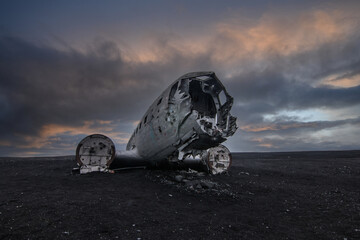 Old plane wreck on black sand in Iceland. Silver colored old airplane without engines on the ground in the evening with dramatic clouds at sunset. Abandoned place on Iceland
