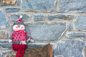 Christmas snowman ornament on wooden trunk and rustic stone background with copy space