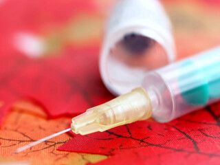 vaccination ampoule with a syringe against Covid-19 or Corona virus on red autumn leafs
