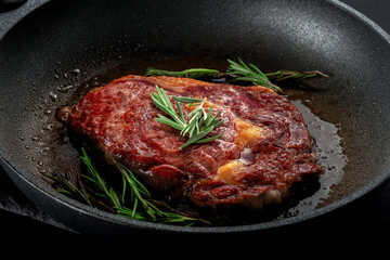Cooking rib eye steak in a frying pan with rosemary. Grilled steak cooked in the kitchen