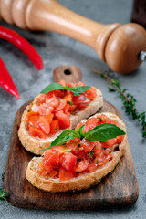 Bruschetta with chopped tomatoes, basil and pesto sauce on wooden board. Toast with ciabatta and tomatoes