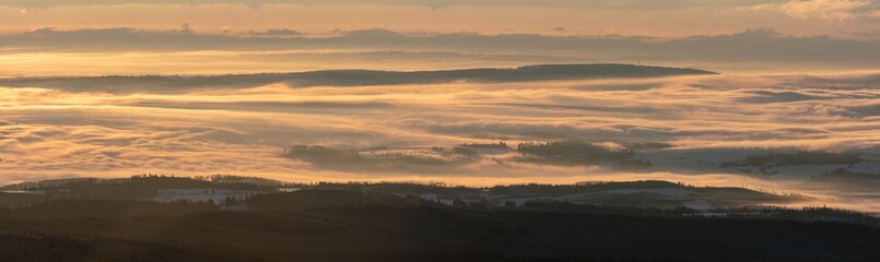 Foggy valley with cloud rolling over the hills at sunrise in winter. Panorama.