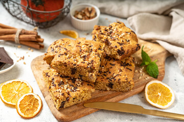 Pumpkin blondie bars with chocolate and walnuts close-up. Brownie pie slices on a serving wooden board on a light gray culinary background. Baking for Thanksgiving	