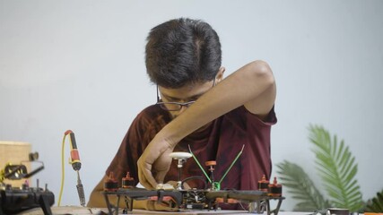 Young man or student making drone by soldering wires to board at home - concept of drone repair and development, scientific experimenting or researching