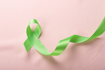 Green ribbon on brown background for Lymphoma Cancer and mental health awareness raising support patient living with illness concept