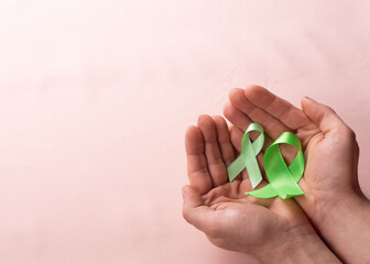 hands holding green ribbon on brown background, children awareness of mental health and lymphoma, world mental and world kidney health day organ donation