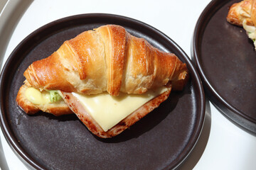 Freshly baked homemade delicious croissant sandwich ham cheese in black plate on wooden breakfast table, top view of breakfast table.
