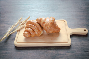 Two freshly baked delicious croissants with spikelets on wooden cutting board, food on breakfast table