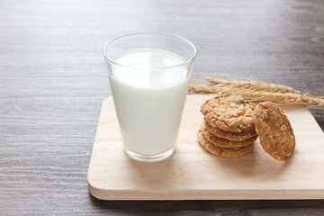 Delicious oatmeal cookies with spikelets and glass of milk on wooden cutting board on table.