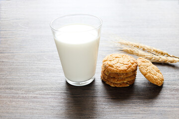 Delicious oatmeal cookies with spikelets and glass of milk on wooden table.